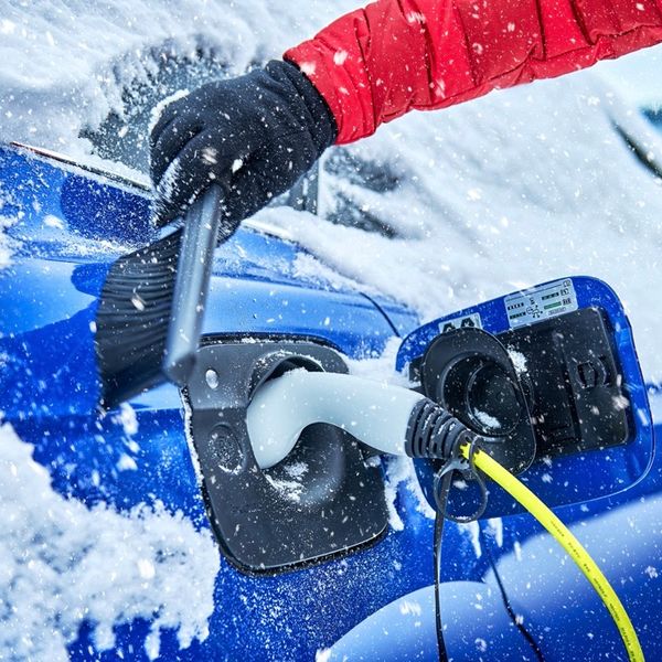 Close up of an electric car charge slot with cable, surrounded by snow and ice with a brush being used to remove snow